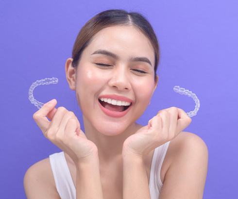 Young woman holding two Invisalign trays and smiling