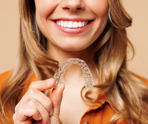 Close up of woman’s smile as she holds an Invisalign tray