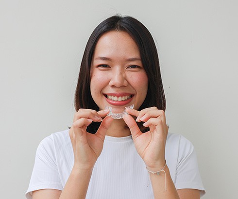 Woman smiling while holding Invisalign aligner