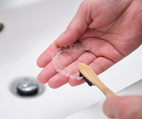 Patient using toothbrush to clean aligner