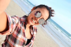 Woman with brown hair in plaid shirt smiling with braces at the beach