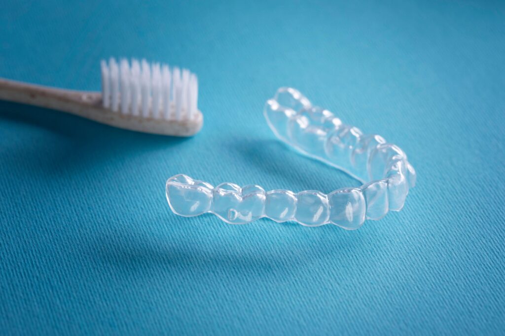 Closeup of wooden toothbrush next to Invisalign on light blue surface